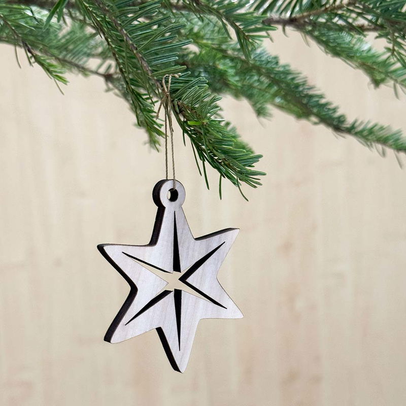 Stjärna i trä, nordisk juldekoration i naturlig stil Trähänge i form av en nordisk stjärna med utskuren mitt, i naturlig björkplywood och hängande i grankvist.