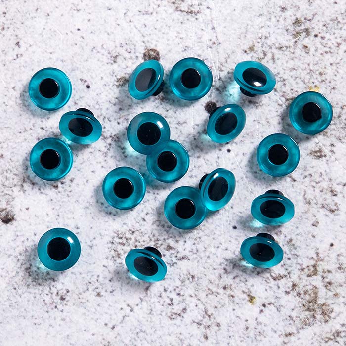 Blå knappögon 12 mm, utspridda på underlag av betong