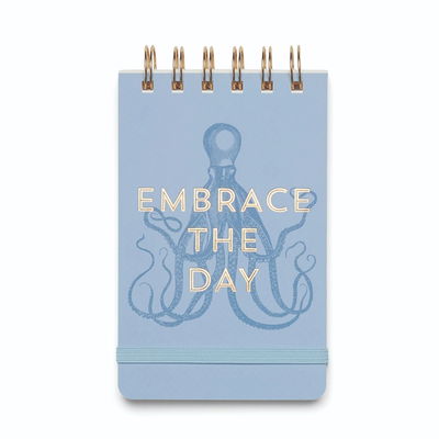 Anteckningsblock med texten Embrace The Day med bläckfiskillustration. Texten och spiralbindningen är i guldfärg