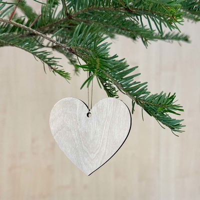 Hjärta i naturfärgat trä upphängt i gran, idealiskt som juldekoration eller för egna målade projekt.