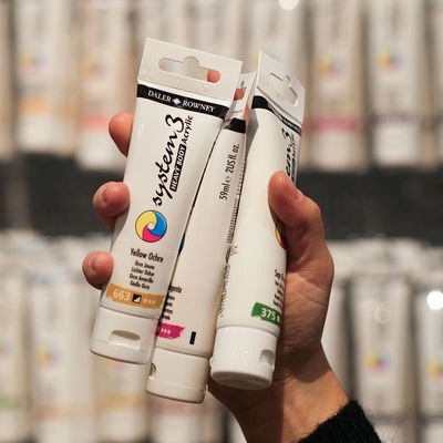 Hand som håller tre tuber Daler-Rowney System 3 Heavy Body akrylfärg i olika kulörer