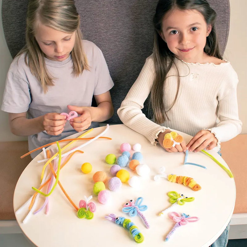 Två barn pysslar med pompoms, piprensare och plastögon och bygger fjärilar och fantasifigurer