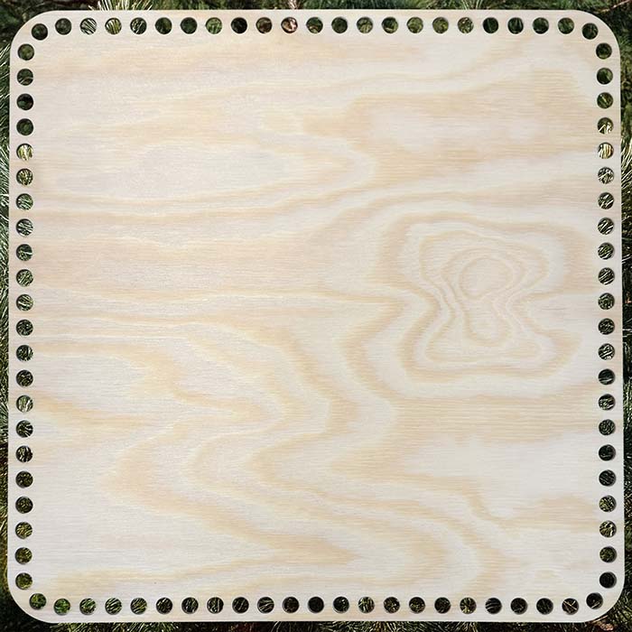 Rund korgbotten, dia. 30x30 cm, i ljus furuplywood med 9 mm hål, placerad mot en bakgrund av gröna tallgrenar.
