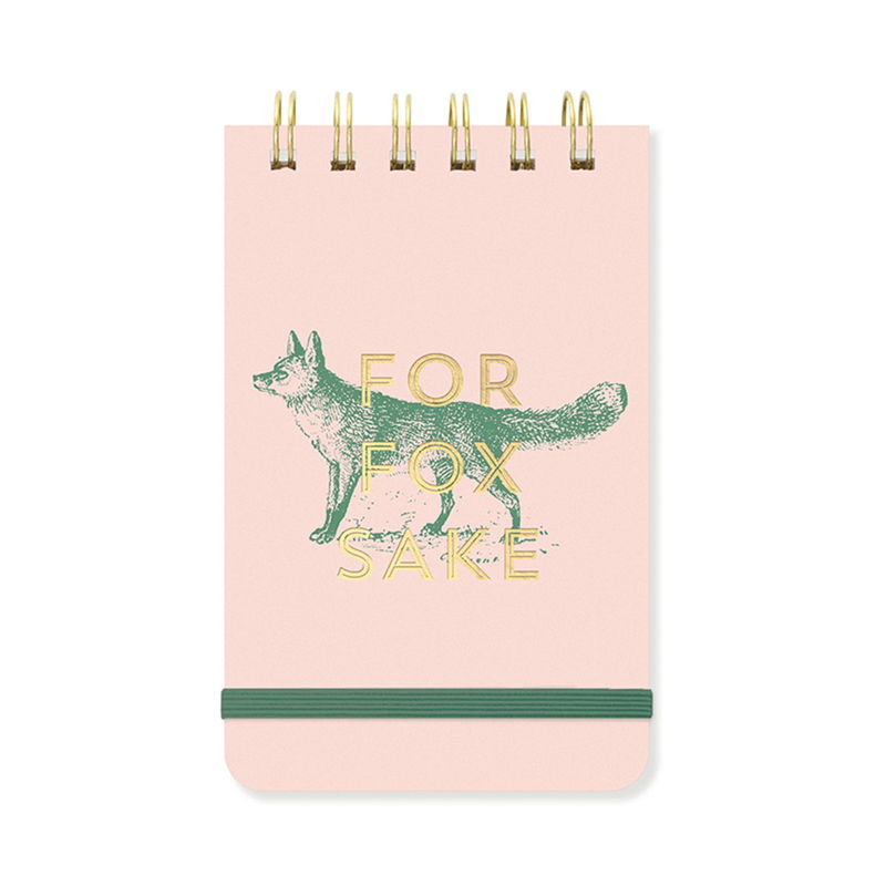 Anteckningsblock med texten For Fox Sake med rävillustration. Texten och spiralbindningen är i guldfärg