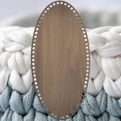 Oval korgbotten till virkning, 20x40cm. Botten är tillverkad av valnötsfanér på träfiberskiva. Bakgrundsbilden är virkat garn