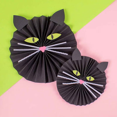 Svart kattfigur vikt av papper med vita piprensare som morrhår och gröna ögon