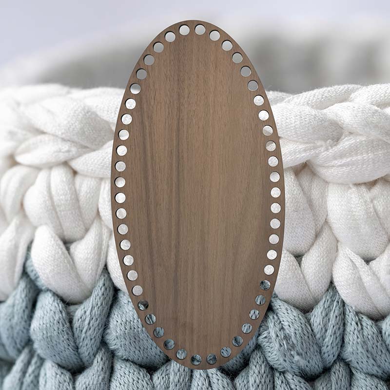 Oval korgbotten till virkning, 15x30 cm. Botten är tillverkad av valnötsfanér på träfiberskiva. Bakgrundsbilden är virkat garn