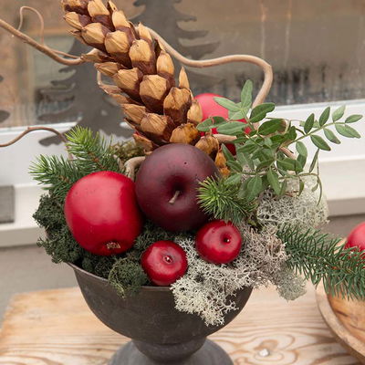 Blomsterarrangemang med mörkröda äpplen, kottar och grön mossa