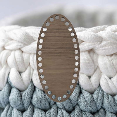 Oval korgbotten till virkning, 10x20 cm. Botten är tillverkad av valnötsfanér på träfiberskiva. Bakgrundsbilden är virkat garn