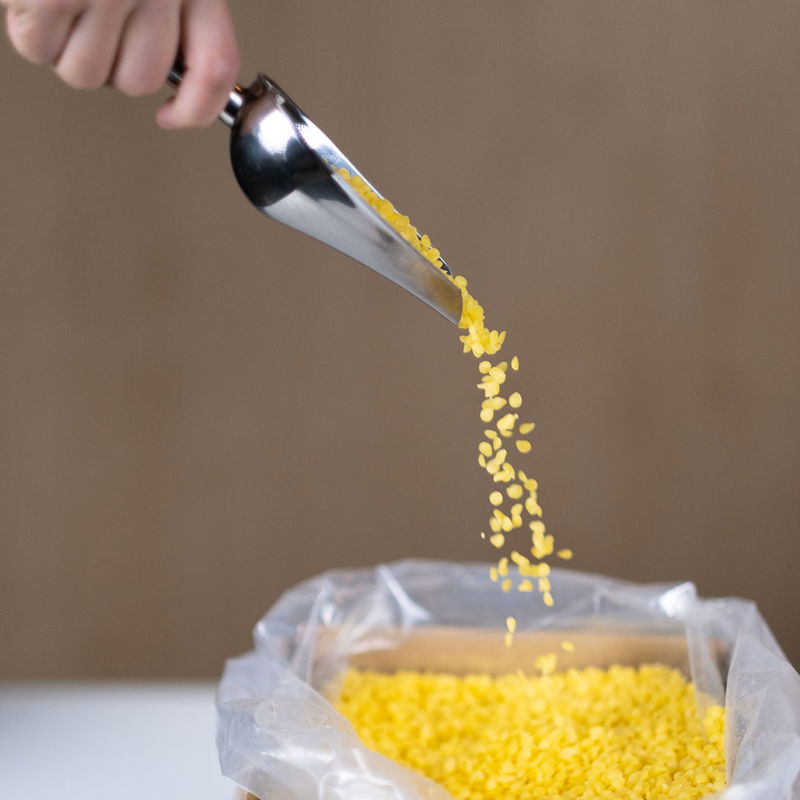 Gult bivax i pellets som hälls från metallskopa