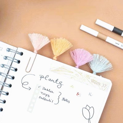 Fyra kopparfärgade gem med tofs i pastellfärger som sidmarkörer i en bullet journal