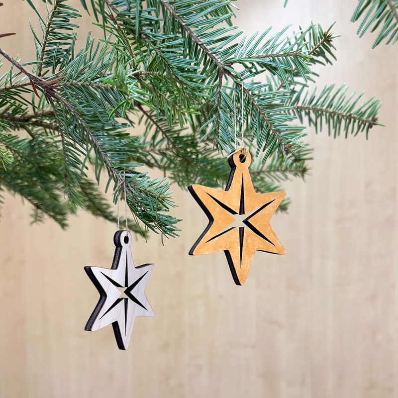 Julhänge Stjärna Nordisk, stilren trädekoration med nordisk känsla Två stjärnformade julhängen i trä, en målad i guld och en i naturlig plywood, hängande i gran