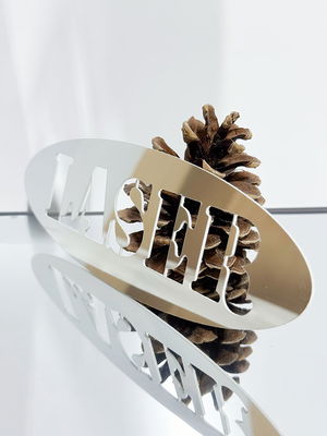 Laserskära spegelsplast HIPS, på bilden en utskuren text och en kotte som reflekteras i plasten