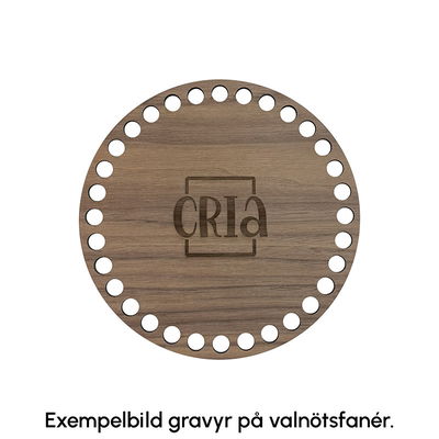 Exempelbild på hur gravyr ser ut på korgbottnar av valnötsfanér. På denna korgbotten är Crias logga graverad