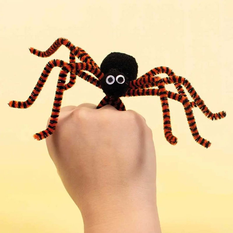 Svart pompom-spindel med orangea och svarta piprensare-ben samt plastögon på hand - halloweenpyssel