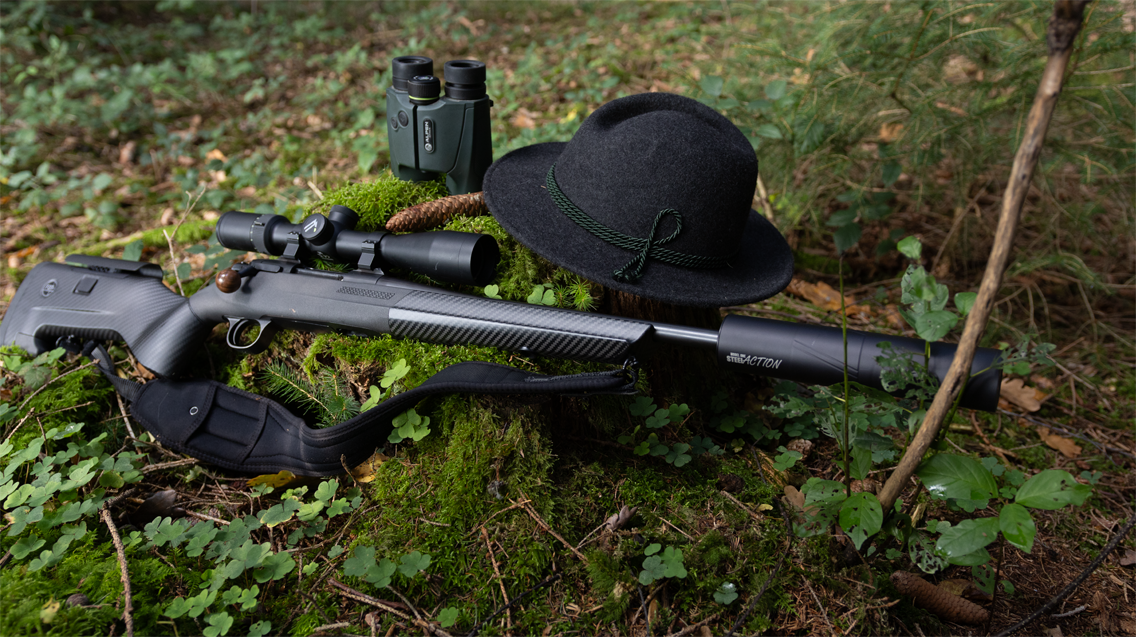 Bild på Steel-action vapensystem med FBT kolv och ett kikarsikte från Alpen Optics monterat uppe på. På bilden syns även en handkikare från Alpen Optics i bakgrunden.