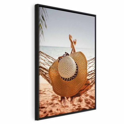 Hammock on the beach – svart ram. En stor stråhatt ligger framför uppsträckta ben i en hängmatta över en varm sandstrand.