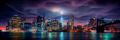 New york dark city – motivvy. Färgade ljus speglas i mörkt vatten framför skyskrapor och en bro i en lång stadsvy.