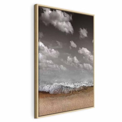Sky wave vertical – naturfärgad ram. Ljusa moln på mörkare grå himmel möter en vit vågkant och en sandfärgad strand i en lodrät komposition.