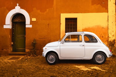 Italian street wide – motivvy. En liten vit bil står på kullersten framför en orange husvägg med mörk dörr och vita detaljer.