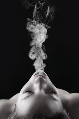 Smoke cloud vertical – motivvy. Ett ansikte lutar bakåt medan en ljus rökpelare stiger upp mot en svart bakgrund.