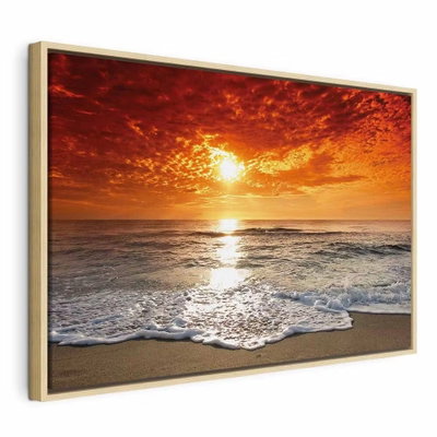 Gorgeous beach – naturfärgad ram. En stark sol sänker sig över havet under orange moln medan en vit skumvåg når sandstranden.