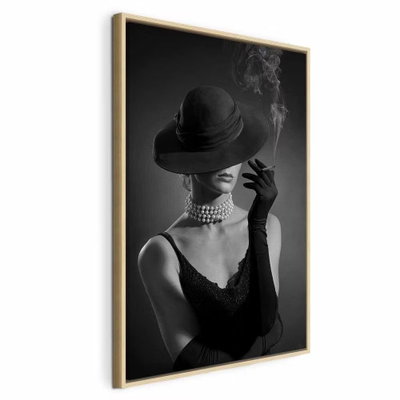 Black elegance vertical – naturfärgad ram. En kvinna i mörk hatt, handskar och pärlhalsband håller en cigarett med en liten rökstrimma mot svart.