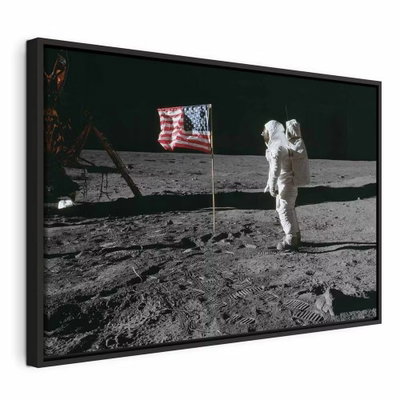 Always first wide – svart ram. En vitklädd astronaut står vid en amerikansk flagga och teknisk utrustning på en grå yta mot svart rymd.