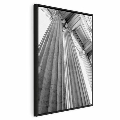 Stone columns vertical – svart ram. Höga, räfflade stenpelare ses nedifrån i svart och vitt med starka linjer mot en ljus himmel.