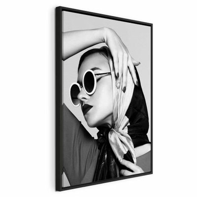 Stylish lady vertical – svart ram. En kvinna med ljus scarf och runda solglasögon håller en hand över huvudet i ett kontrastrikt svartvitt porträtt.