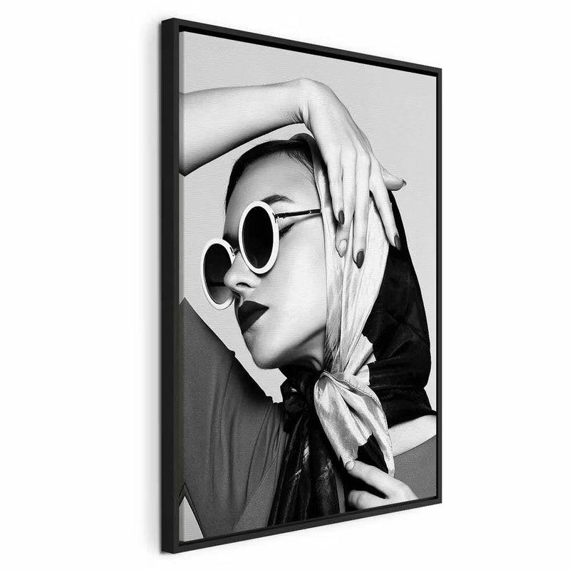 Stylish lady vertical – svart ram. En kvinna med ljus scarf och runda solglasögon håller en hand över huvudet i ett kontrastrikt svartvitt porträtt.