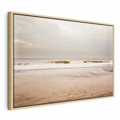 Sea after storm wide – naturfärgad ram. Små vågor möter en bred sandstrand under en stor, ljus himmel i beige och grå toner.
