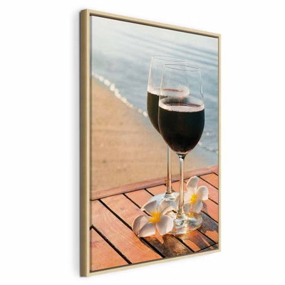 Love refreshment vertical – naturfärgad ram. Två glas med mörk dryck står på ett träbord med ljusa blommor framför en sandstrand och lugnt vatten.