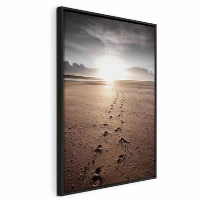 Our way vertical – svart ram. Fotspår leder genom mörk sand mot ett ljust solparti över havet under en grå himmel.