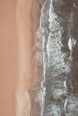 Shore line vertical – motivvy. En smal vit vågkant skiljer grågrönt vatten från en bred sandfärgad strand i en vy ovanifrån.