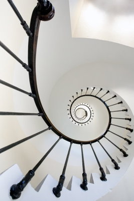 Endless stairs vertical – motivvy. En vit spiraltrappa med mörkt räcke slingrar sig in mot en liten rund mittpunkt.