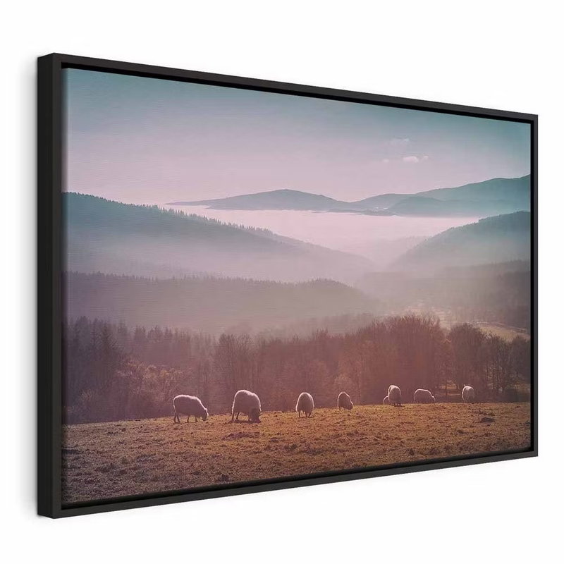 Sheep in mountain landscape – svart ram. Små får betar på ett fält nedanför skogsklädda berg med rosa och grå dimma mellan höjderna.