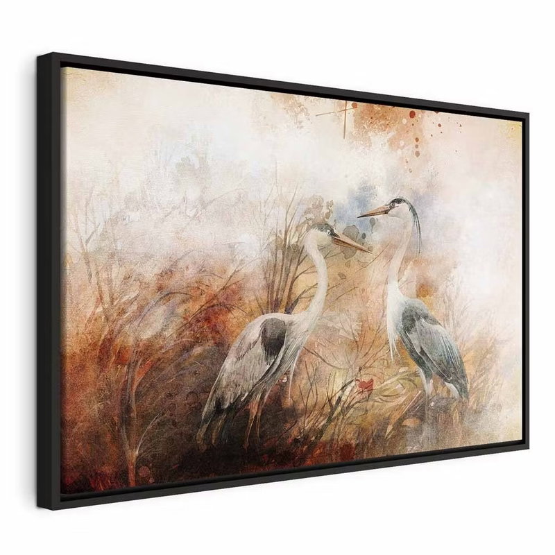 Herons on the hunt wide – svart ram. Två gråvita hägrar står i högt gräs återgivet med lösa penseldrag i brunt, orange och crème.