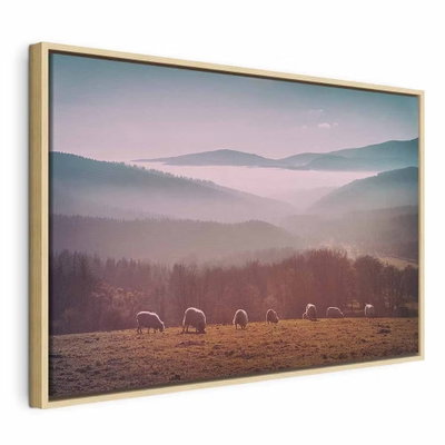 Sheep in mountain landscape – naturfärgad ram. Små får betar på ett fält nedanför skogsklädda berg med rosa och grå dimma mellan höjderna.