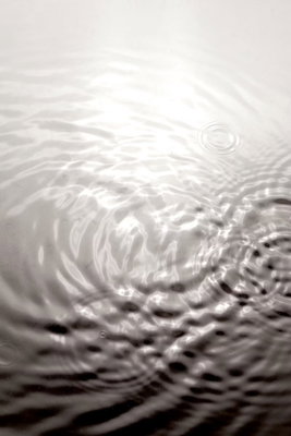 Water surface vertical – motivvy. Runda ringar breder ut sig över en vattenyta i ett motiv med svarta, vita och grå toner.