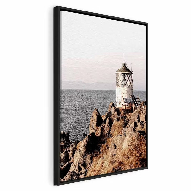 Lantern on the cliff – svart ram. En liten vit fyr står på en brant klippa vid ett lugnt hav under en ljus himmel.