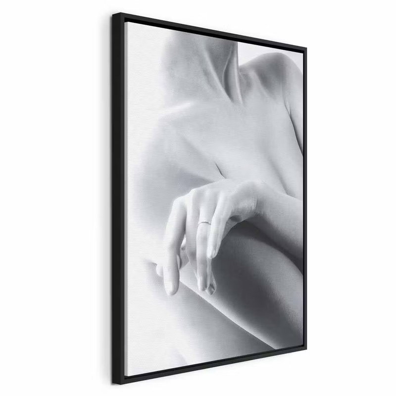 Feminine delicacy vertical – svart ram. En ljus hand vilar mot en naken axel i ett mjukt beskuret svartvitt fotografi.