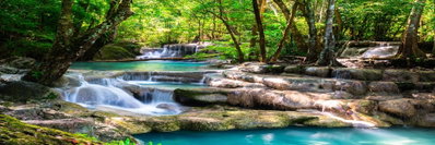 Nature forest waterfall – motivvy. Ljust vatten rinner i flera små fall över stenar i en tät grön skog.