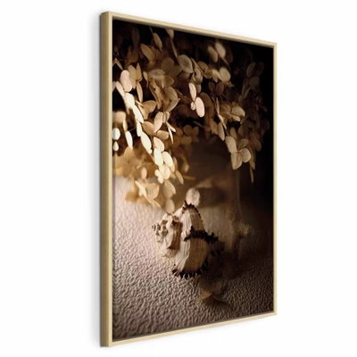 Humming seashell vertical – naturfärgad ram. En liten snäcka ligger framför ett kärl med ljusa, torra blad i varmt sidoljus.