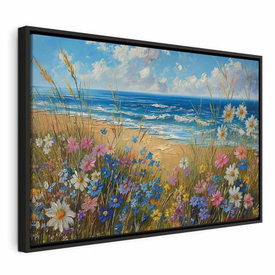 Seascape wildflowers and a – svart ram. Vita, rosa och blå ängsblommor växer framför en sandstrand och ett blått hav under ljus molnhimmel.