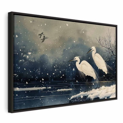 Herons over a winter pond – svart ram. Två vita hägrar står vid mörkt vatten med snö på grenarna och små ljusa flingor i luften.