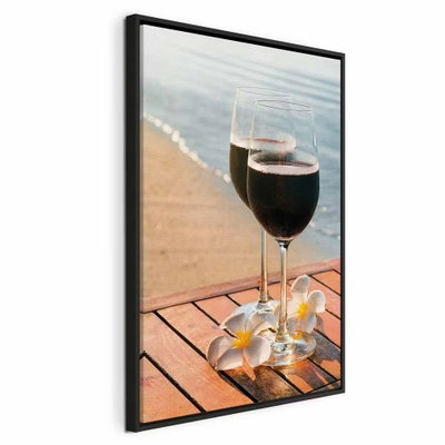 Love refreshment vertical – svart ram. Två glas med mörk dryck står på ett träbord med ljusa blommor framför en sandstrand och lugnt vatten.
