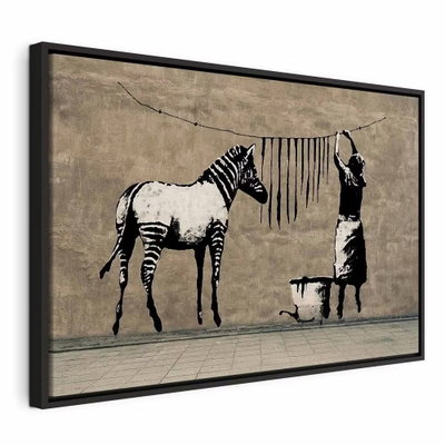 Banksy washing zebra on – svart ram. En zebra står intill en person som hänger mörka ränder på en tvättlina i ett svartvitt väggmotiv.