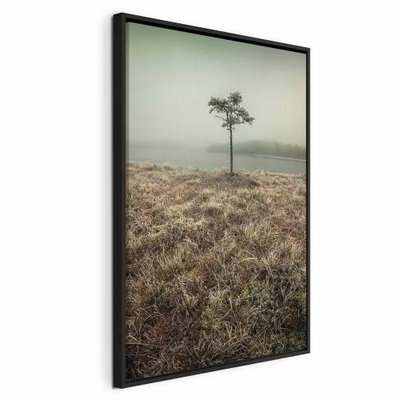 At the lake shore vertical – svart ram. Ett litet ensamt träd står i ett brunt gräsfält framför en dimmig sjö och en blek grågrön himmel.