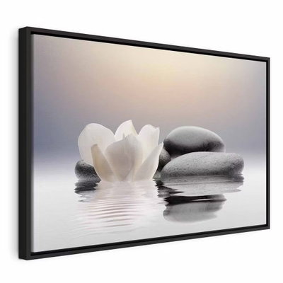 Garden of calm – svart ram. En vit blomma ligger intill staplade, rundade grå stenar som speglas i en stilla vattenyta.